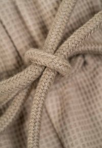 Cuerda trenzada beige con un nudo, sobre un fondo texturizado de un beige claro. El material está tejido y parece duradero.