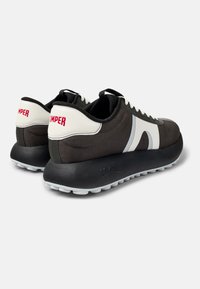 Sneaker bianco e nero con tomaia in rete, punta rotonda, motivo a onde in contrasto e suola stratificata con impugnature circolari bianche.