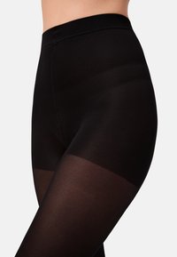 Zwarte leggings met een gladde, ondoorzichtige textuur. Beschikt over een hoge taille en een lichte doorschijnendheid bij het onderbeen, wat een gradient-effect geeft.
