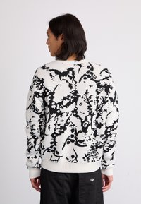 Textured knit sweater in white with black floral patterns. Crew neck, ribbed cuffs, and hem. Relaxed fit and long sleeves.