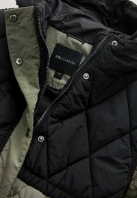 Kurta danga, turinti juodą išorinį sluoksnį, šviesiai žalią pamušalą, sidabrinius aksesuarus ir logo etiketę. Uždarymas su užtrauktuku ir spaustukais.