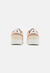 Baskets en cuir rose et beige avec une semelle en caoutchouc blanc, présentant une texture douce et une languette en tissu au talon. Logo à l'arrière.