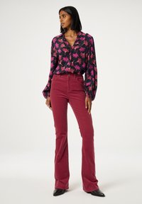 Zwart blouse met bloemmotief en diepe roze bladeren, gecombineerd met bordeauxrode flared corduroypantalon en zwarte enkellaarsjes.