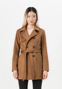 Manteau trench en marron à double boutonnage en tissu doux. Présente une taille à nouer, des poches latérales et un col cranté ; texture lisse et design ajusté.