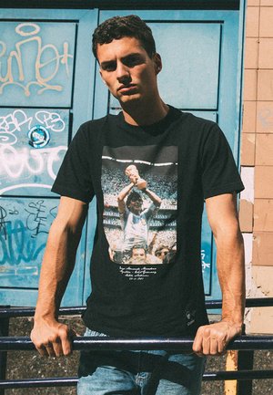 Zwarte katoenen t-shirt met een grafische print van een feestelijke figuur die een trofee vasthoudt, met witte tekst en een klassieke pasvorm.