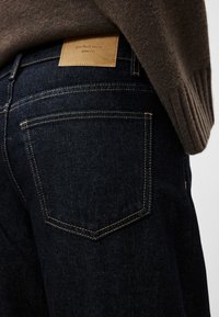 Μπλε σκούρο τζιν με απαλό υφή, που διαθέτει ετικέτα από ταμπά δέρμα και κίτρινη ραφή στις τσέπες.