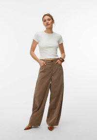 Haut blanc à manches courtes associé à un pantalon large en velours côtelé marron. Des talons en cuir marron à bout pointu complètent la tenue. Texture lisse dans l'ensemble.