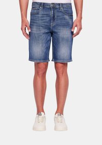 Shorts in denim blu chiaro con una finitura scolorita, taglio dritto, cinque tasche e vita standard, abbinati a scarpe da ginnastica bianche.