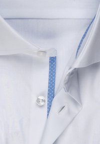 Chemise blanche avec un accent à motif bleu au niveau du col, dotée d'un bouton en plastique et de coutures détaillées sur la patte de boutonnage interne.
