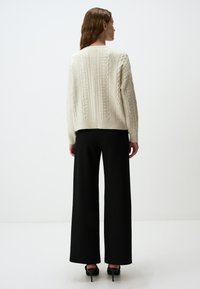 Crème kabelgebreide trui met een ontspannen pasvorm, gecombineerd met zwarte high-waisted wijde broek. Soepele textuur en geribbelde details.