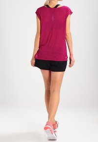 Fuchsiové atletické tričko s krátkými rukávy, v kombinaci s černými šortkami a červenými teniskami, s texturovaným povrchem a decentním detailem na zádech.