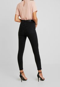 Farkkuhousut mustat korkeavyötäröiset skinny-mallit, joissa on siisti muotoilu, hieman joustavuutta ja kaksi takataskua. Yhdistetty vaaleanpunaiseen lyhythihaiseen toppiin.