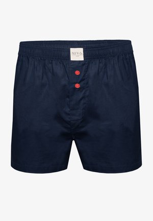 Bañadores de algodón azul marino con una textura suave, cinturilla elástica y tres botones rojos en la parte delantera. Etiqueta cosida en el interior de la cinturilla.