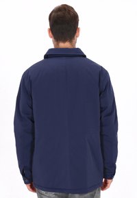 Chaqueta azul marino con cuello, mangas largas y textura lisa. Cuenta con puños con botones y dobladillo trasero recto.