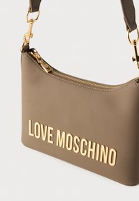Τσάντα χειρός από μπεζ συνθετικό δερμάτινο υλικό με φερμουάρ, χρυσά μεταλλικά στοιχεία και ανάγλυφο λογότυπο "LOVE MOSCHINO" στο μπροστινό μέρος για εντυπωσιακή λεπτομέρεια.