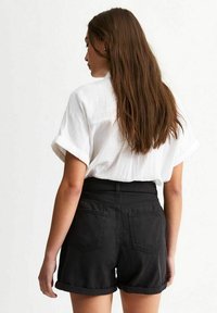 Black high-waisted shorts with rolled cuffs and two back pockets, paired with a loose-fitting white textured shirt.