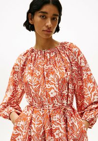 Robe à imprimé floral en orange et blanc, avec un col froncé, des manches longues, une taille cintrée et un tissu doux et léger.