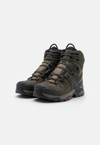 Buty trekkingowe z ciemnozielonym materiałem i czarnymi gumowymi akcentami. Posiadają solidny system sznurowania, wzmocnione noski oraz teksturowane podeszwy zapewniające dobrą przyczepność.
