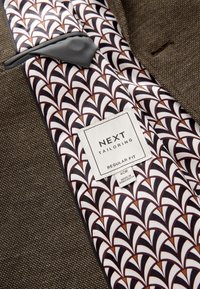 Veste de costume marron texturée sur mesure avec doublure en soie à motifs présentant un design géométrique et une étiquette indiquant « NEXT Tailoring Regular Fit 40R ».
