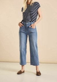 T-paita, jossa on tummansiniset ja valkoiset raidat, paritettu vaaleansinisten leveälahkeisten farkkujen ja ruskeiden liukuvaatteiden kanssa. Sujuva kangas ja rento istuvuus.