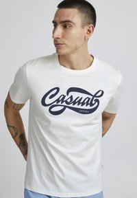 Baltos medvilnės marškinėliai su išsiskiriančiu tamsiai mėlynu užrašu "Casual Friday". Trumpomis rankovėmis, apvaliu kaklu ir minkšta tekstūra.