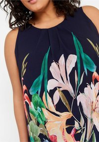 Ärmlös klänning i marinblått tyg, med en livlig blommig tryck i nyanser av rosa, grönt och orange. Plisserad halsringningsdetalj.