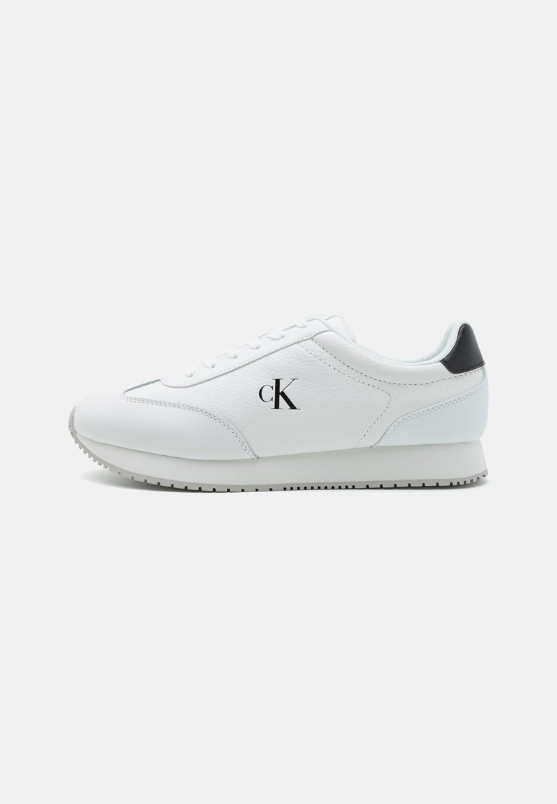 Witte leren sneaker met een gestructureerde afwerking, vetersluiting en een zwarte hielaccent. Heeft een klein "cK"-logo aan de zijkant. Platte rubberen zool.