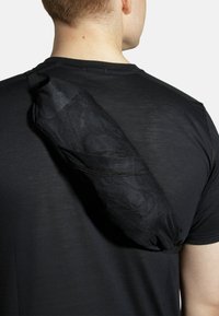 Sort mesh sling taske, cylindrisk form, fastgjort til skulderen, har elastisk lukning og en tekstureret overflade for bedre greb.
