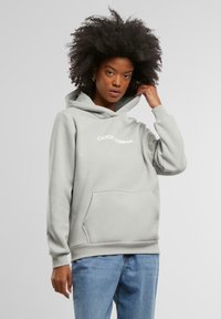 Ljusgrå hoodie med ficka fram och dragsko i huvan. Utskrivet "GOOD KARMA" i vit text över bröstet. Material av bomullsblandning.