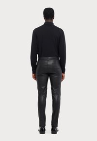Černá dlouhá košile s dlouhým rukávem v kombinaci s přiléhavými černými koženými kalhotami. Outfit se vyznačuje hladkými texturami a minimalistickými designovými prvky.