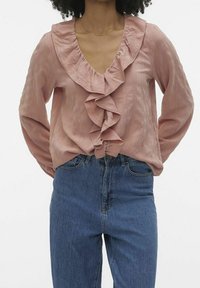 Blouse rose avec col à volants, manches longues et tissu texturé, associée à un jean bleu taille haute à coupe décontractée.
