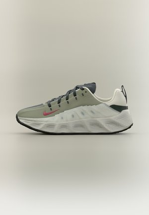 Vaaleanharmaa ja valkoinen urheilukenkä, jossa mustat nauhat, punainen Nike-swoosh-logo, paksu kuvioitu valkoinen pohja ja musta ulkopohja neutraalilla taustalla.