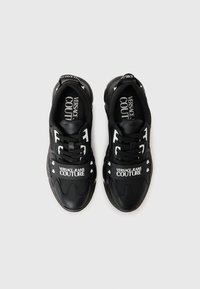 Sorte sneakers med en kombination af læder og stof, med hvid 'VERSACE JEANS COUTURE' branding og markante detaljer på siderne.