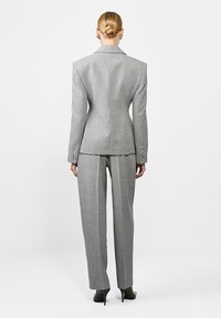 Szary dopasowany garnitur z wyraźnymi ramionami, slim-fit spodniami i teksturowanym materiałem. Guziki na rękawach dodają szczegółów; czółenka na wysokim obcasie dopełniają wygląd.