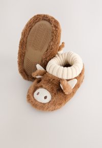 Chaussons marron en peluche avec un motif de vache, dotés d'un col en tissu rayé doux et d'une semelle en caoutchouc texturée pour une meilleure adhérence. Accentués par des oreilles et des yeux.