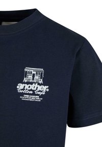 Camiseta de algodón azul marino con cuello redondo, que presenta gráficos impresos en blanco de un café y texto en la parte izquierda del pecho. Textura suave y lisa.