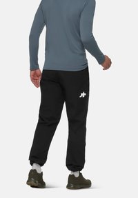 Zwarte broek met een wit logo op de linker dij, gecombineerd met een grijze top met lange mouwen. Zachte stof, slank model, elastische manchetten en hardloopschoenen.