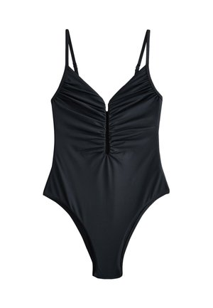 Zbliżenie osoby w czarnym bodysuit z wysokim wycięciem, pokazujące bok tułowia, biodro oraz górną część uda na neutralnym tle.