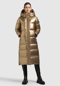 Giacca imbottita dorata con silhouette lunga, design trapuntato, cappuccio oversize, zip frontale e due tasche laterali. Abbinala a stivali neri al ginocchio.