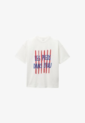 T-shirt blanc à manches courtes avec texte français bleu "Les Pieds Dans L'eau" sur cinq lignes verticales de coups de pinceau rouges à l’avant.