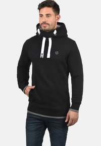 Zwarte sweatshirt met een hoge hals, witte trekkoorden en een klein logo. Heeft een grijze zoom en manchetten, gemaakt van een zachte stof.