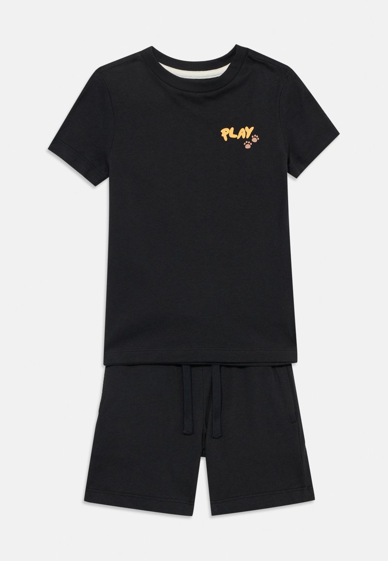 Μαύρο κοντομάνικο T-shirt με το κείμενο «PLAY» και κίτρινα αποτυπώματα πατούσας στο στήθος, σε συνδυασμό με μαύρα σορτς με κορδόνι.