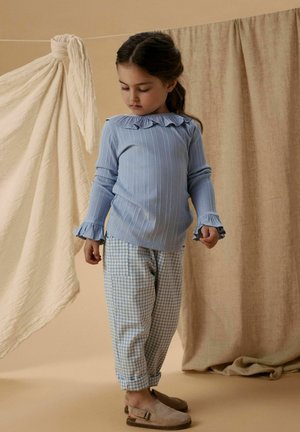 Light blue striped long-sleeve shirt with ruffled collar, paired with checkered blue and white pants. Soft beige shoes complete the outfit.