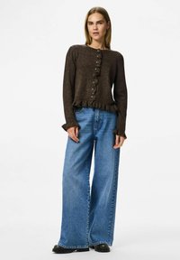 Brun, texturerad cardigan med volangkant och knäppning, kombinerad med vida blå denimbyxor och svarta stövlar.