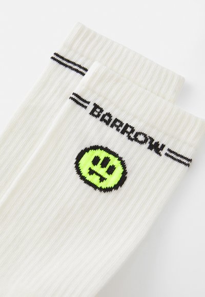 Calzini bianchi a costine con strisce nere e la parola "BARROW." Presentano un emblema di faccina sorridente verde sul fronte.