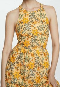 Abito giallo senza maniche con motivi floreali in arancione e verde, caratterizzato da un corpetto aderente e una vita raccolta per una gonna ampia.