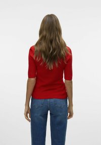 Röd stickad topp med korta ärmar, åtsittande design, ribbad textur. Matchas med högmidjade blå denimjeans. Enfärgad vit bakgrund.