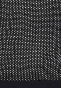 Strikket stof med et struktureret mønster af hvide prikker på en mørk baggrund, der har en blød, glat tekstur og en tætsiddende sort kant.