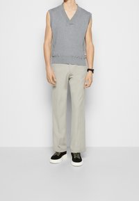 Suéter sin mangas de canalé gris con escote en V, combinado con pantalones de pierna ancha gris claro y zapatillas negras con suelas blancas y detalles en verde.