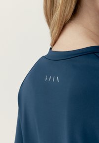 Mörkblå idrottströja med en mjuk yta och rundad halsringning, med minimalistisk vit branding på baksidan.